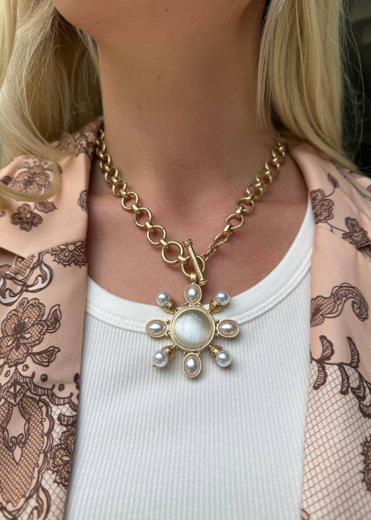 Gold necklace with a sunflower pendant worn by a person