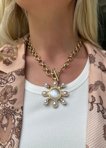 Gold necklace with a sunflower pendant worn by a person