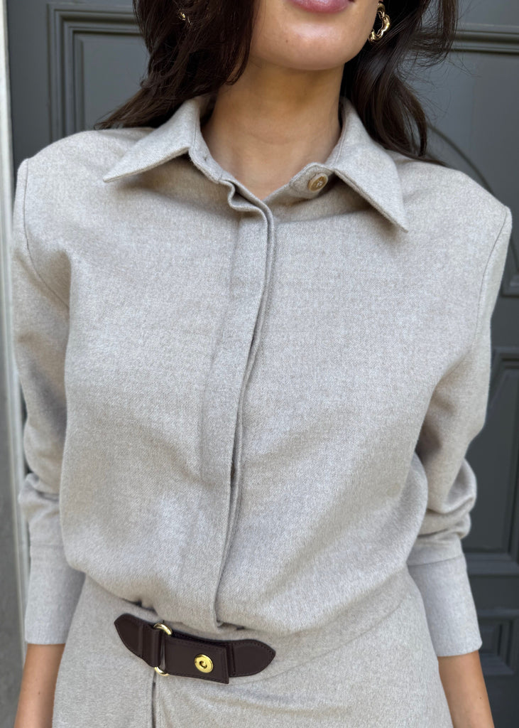 Person wearing a light gray long-sleeve shirt with a belt against a dark background