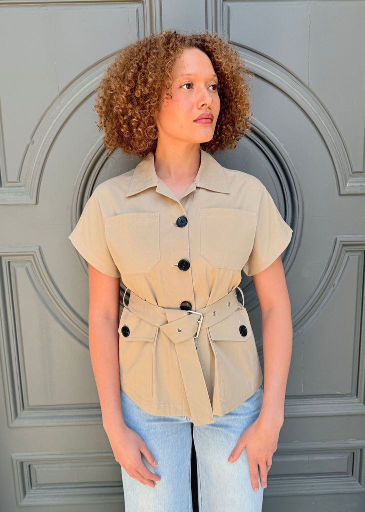Woman wearing a beige short-sleeve shirt with black buttons in front of a gray door.
