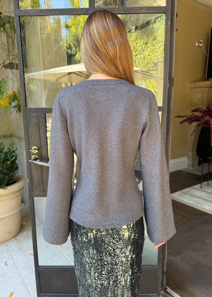 Person wearing a gray sweater and sequin skirt standing in a doorway.