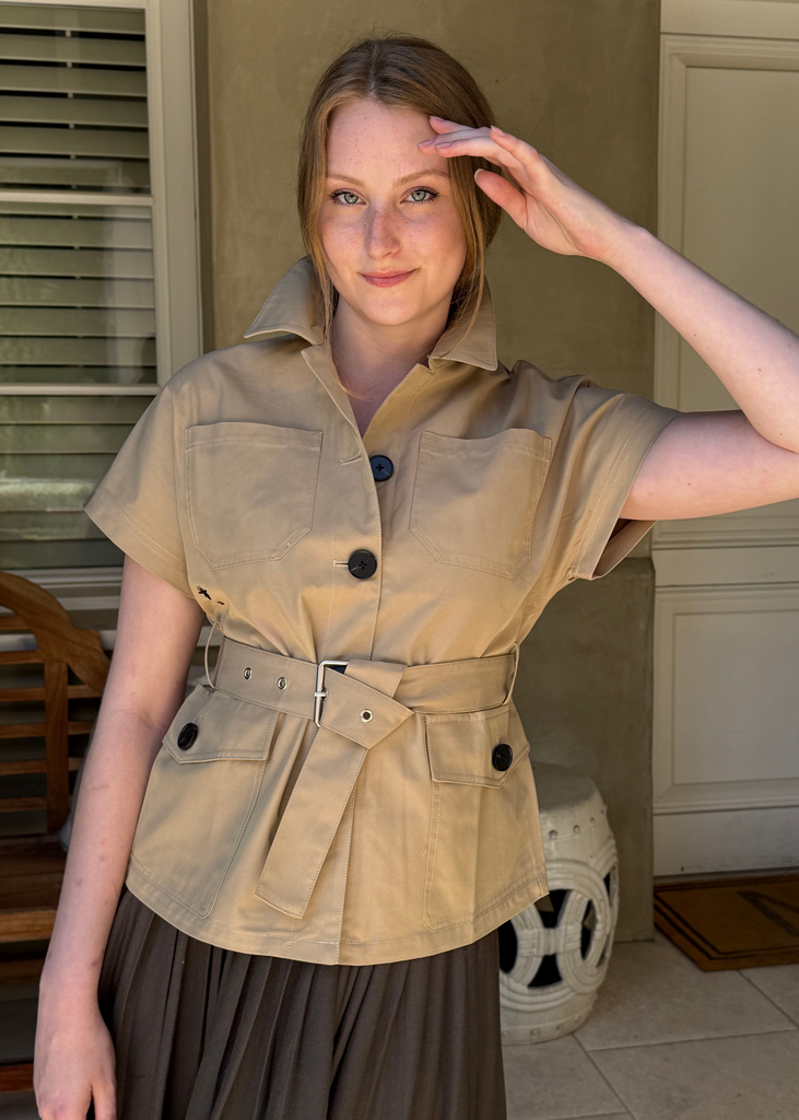 Woman wearing a beige trench coat saluting indoors.