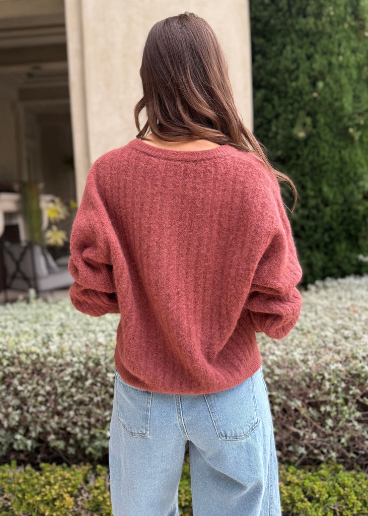 Person wearing a pink sweater and light blue jeans standing outdoors.