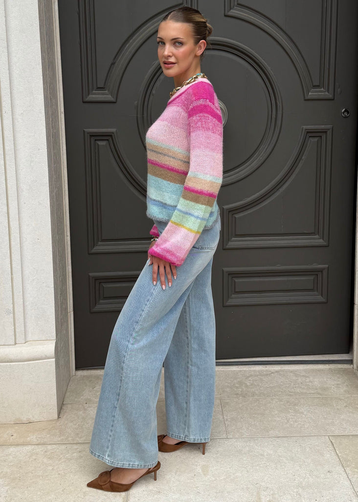 Woman wearing a colorful sweater and light blue jeans standing in front of a dark door.