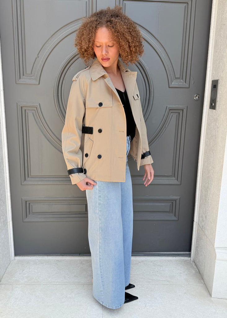 Person wearing a beige trench coat standing in front of a gray door.