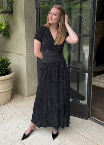 Woman in a black dress standing outdoors next to a building with plants.