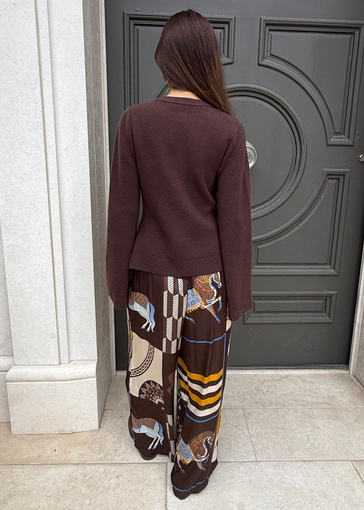Person standing in front of a large ornate door wearing a maroon sweater and patterned pants.