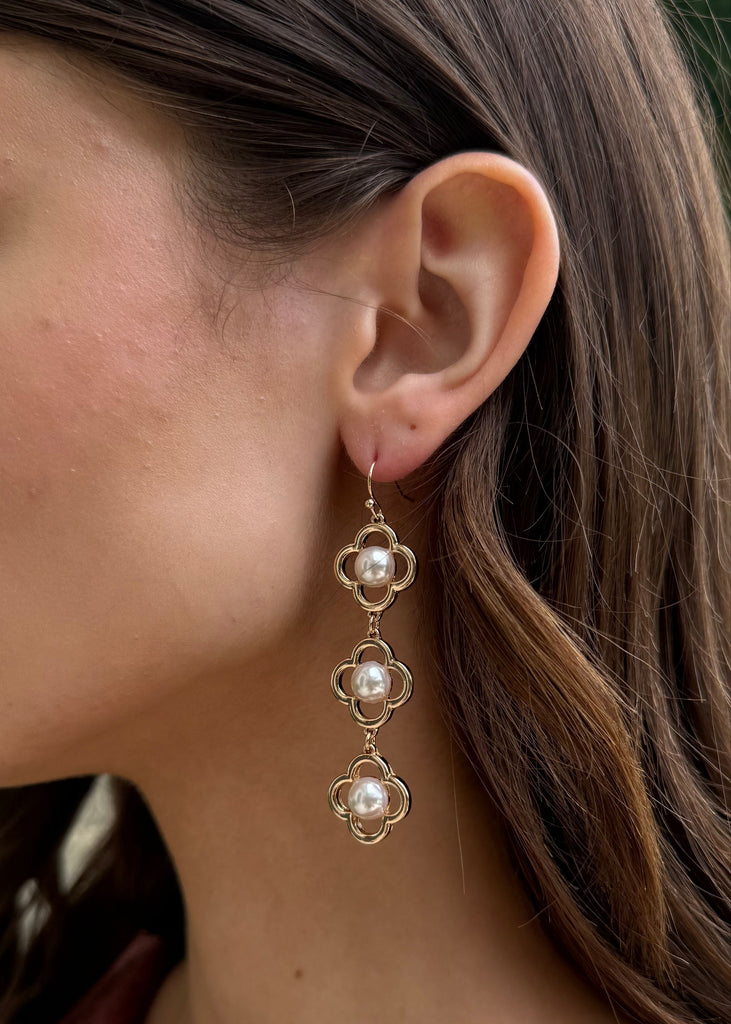 Close-up of a woman wearing a gold earring with pearls, outdoors.