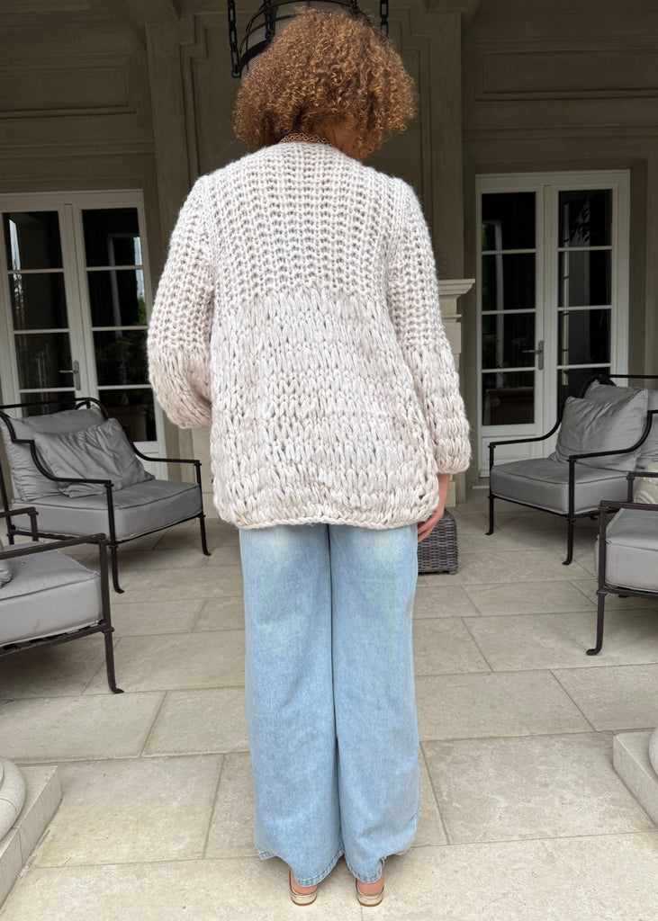 Person wearing a textured cardigan and light blue jeans on a patio.
