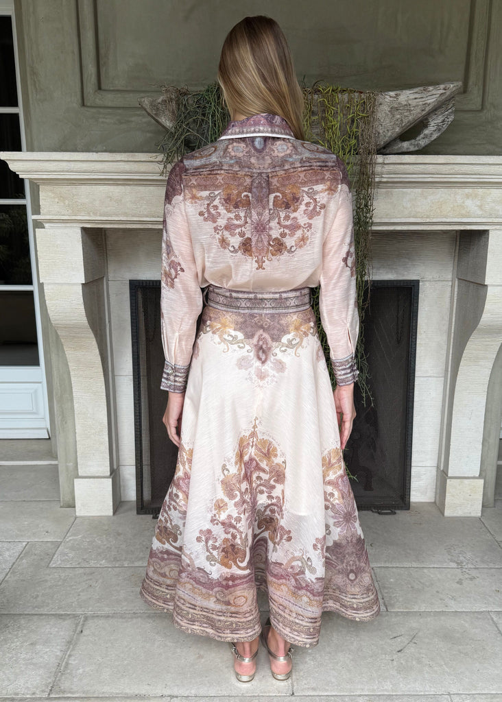 Woman wearing a floral dress standing in front of a fireplace.