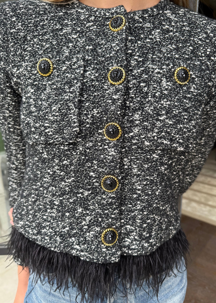 Black and white textured jacket with gold buttons worn by a person indoors.