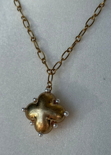 Gold necklace with a clover-shaped pendant on a light gray background