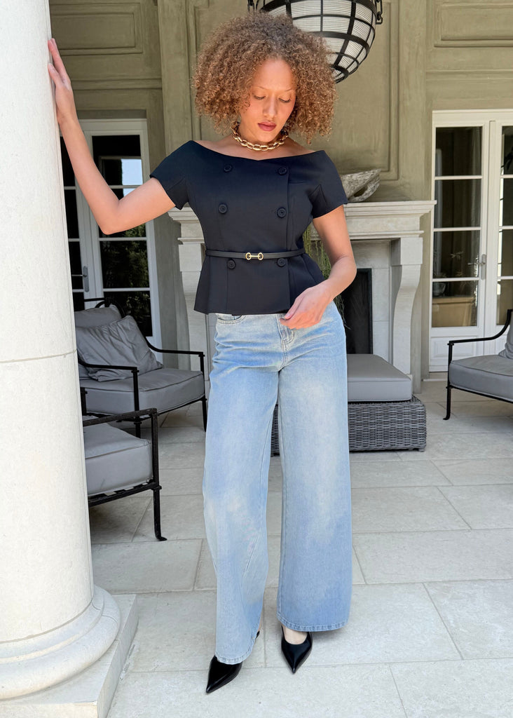 Woman in black top and light blue jeans standing in a stylish outdoor setting.
