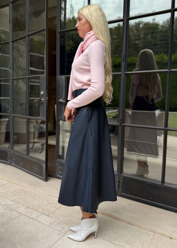Woman in a pink sweater and navy skirt standing in front of a glass door.