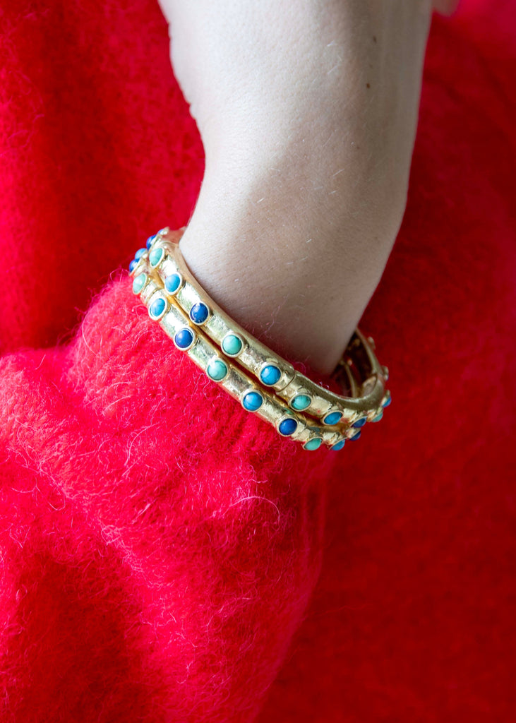 Hand wearing a gold bracelet with blue stones on a red background