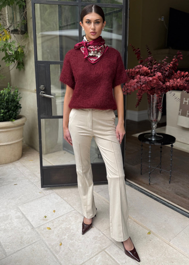 Woman in burgundy sweater and beige pants standing in front of a glass door.