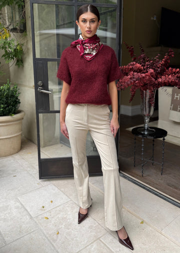 Woman in burgundy sweater and beige pants standing in front of a glass door.