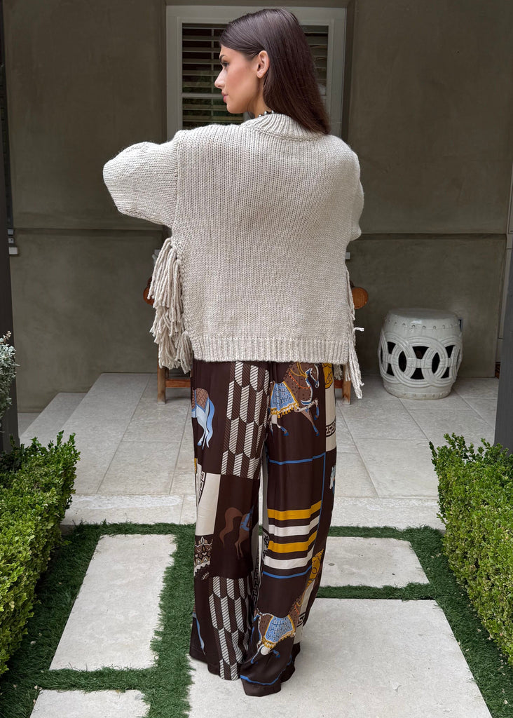 Person wearing a white cardigan and patterned pants standing on a garden path.