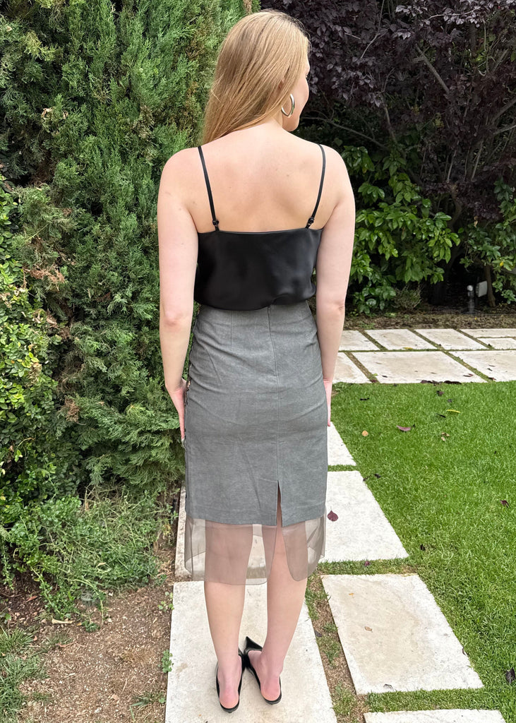 Woman wearing a black top and gray skirt walking on a garden path.