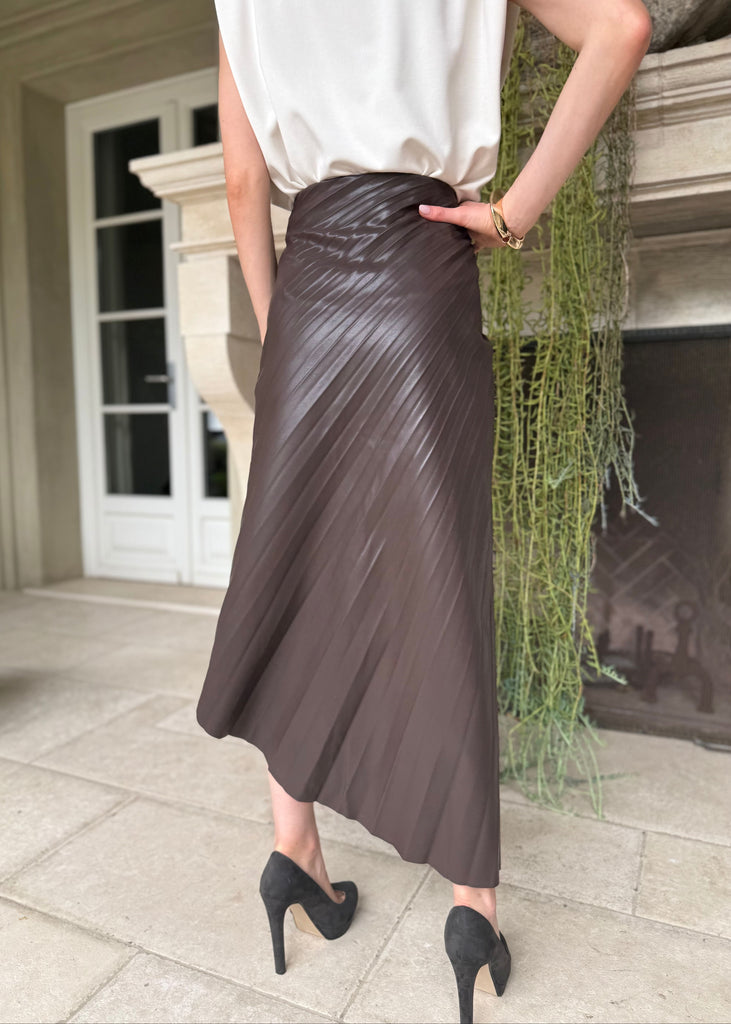 Person wearing a brown pleated skirt and black high heels in an outdoor setting.