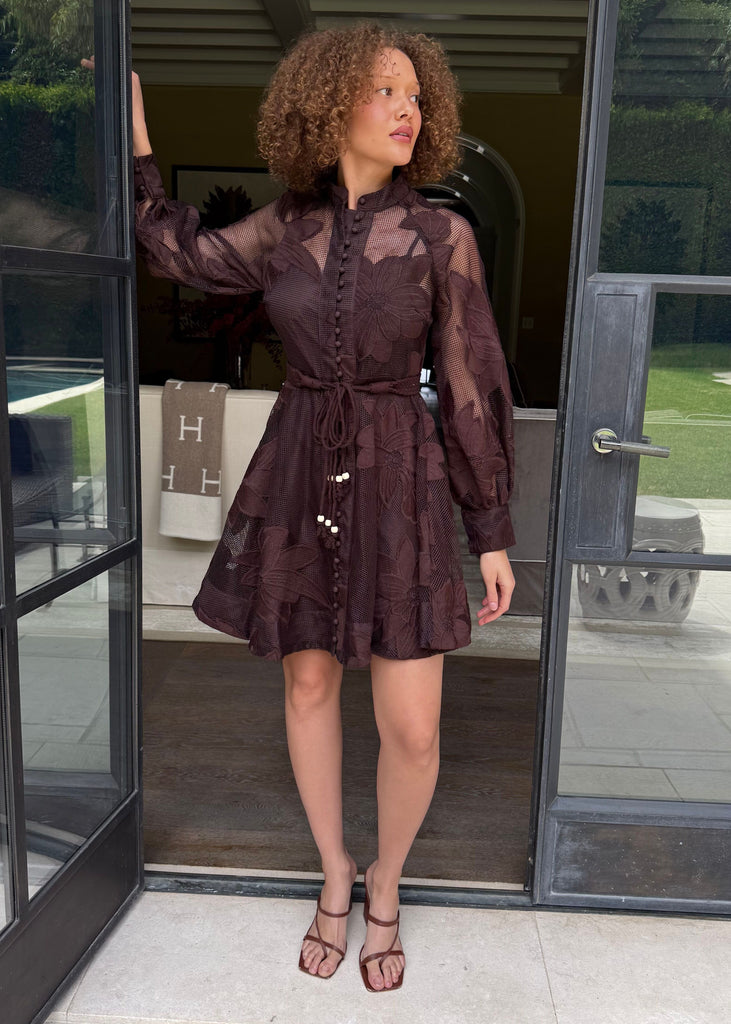 Woman in a dark brown dress standing in front of a glass door.