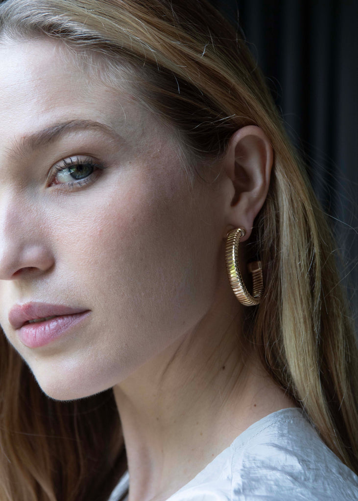 Close-up of a woman wearing gold hoop earrings with a neutral background