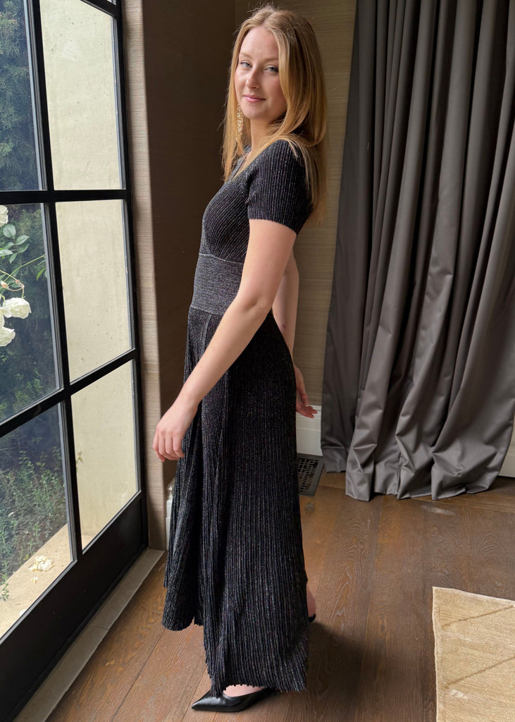 Woman in a black dress standing by a large window with curtains.