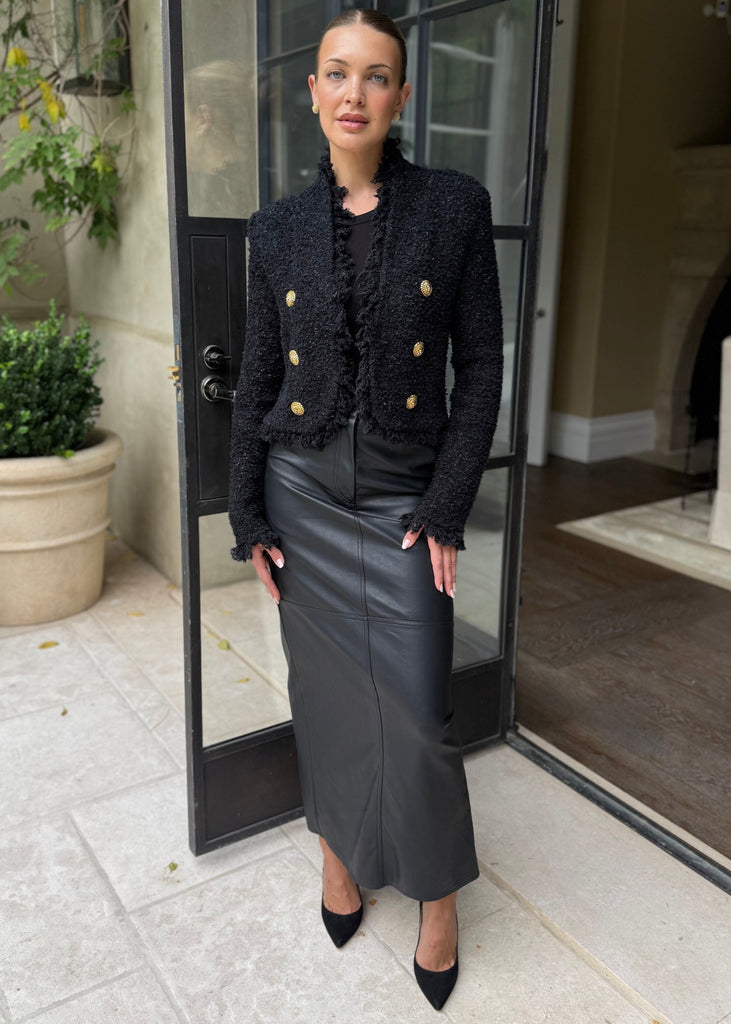Woman in a black outfit standing in a modern interior setting with plants and a glass door.