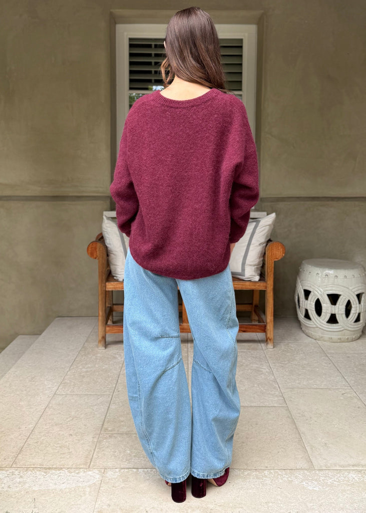 Person wearing a maroon sweater and blue jeans standing on a patio.