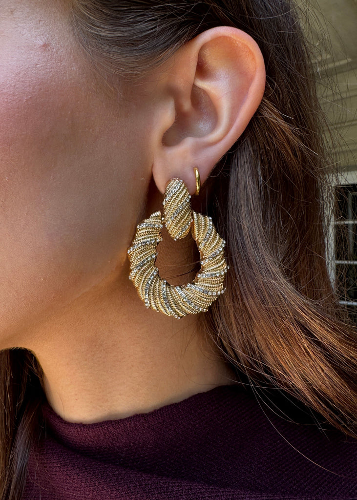 Close-up of a person wearing a gold hoop earring with a blurred background