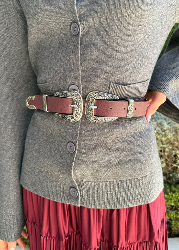 Person wearing a gray cardigan with a red skirt and brown belt outdoors.