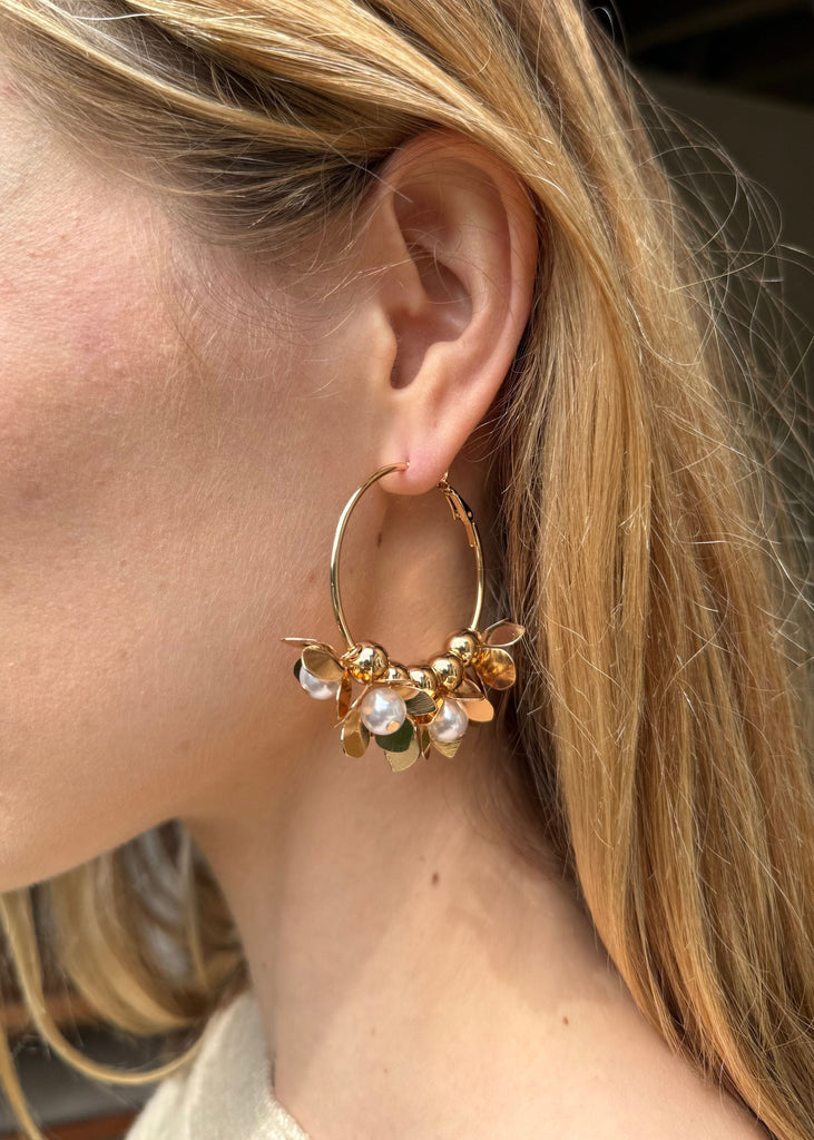 Close-up of a person wearing a gold hoop earring with small embellishments.