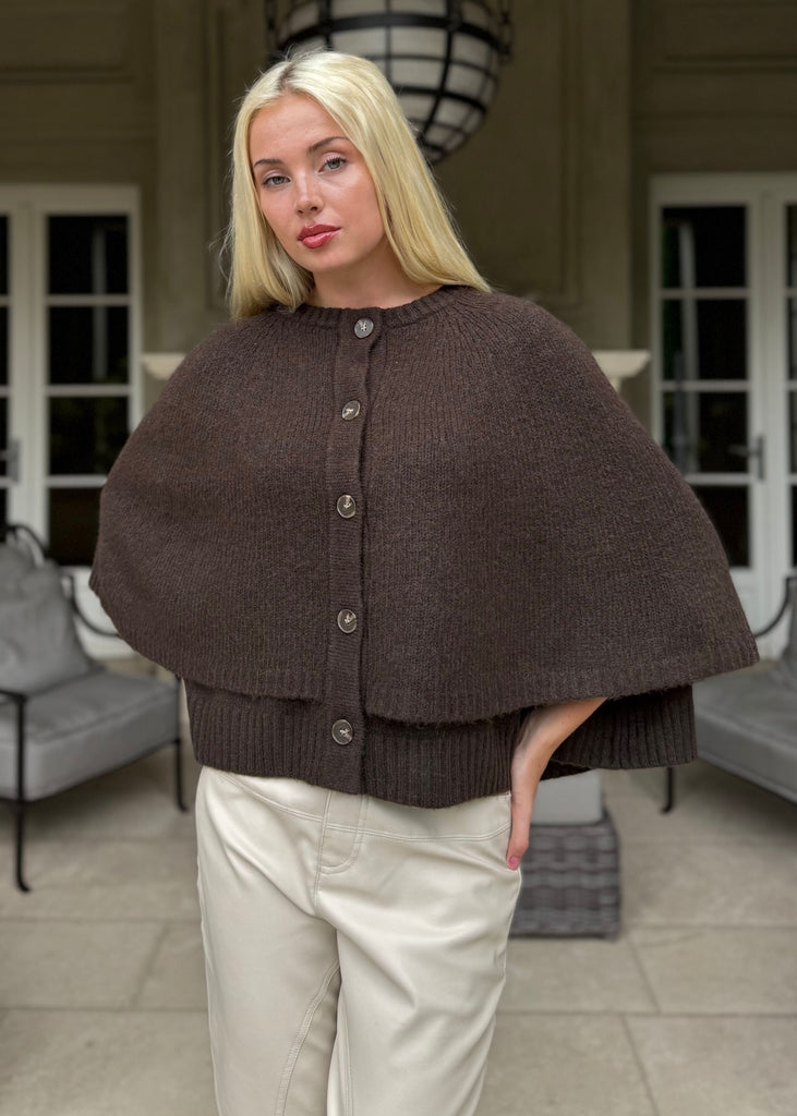 Woman wearing a brown knitted cape in an elegant indoor setting