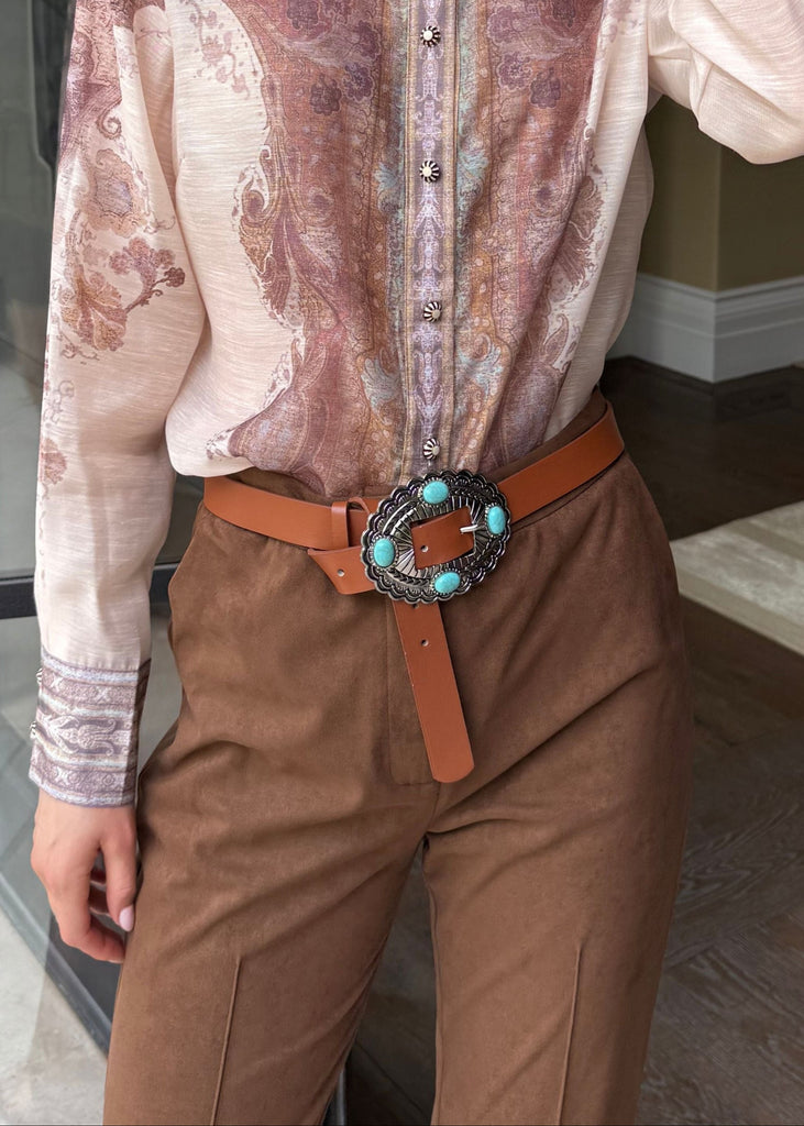 Woman wearing a patterned blouse and brown pants in an indoor setting