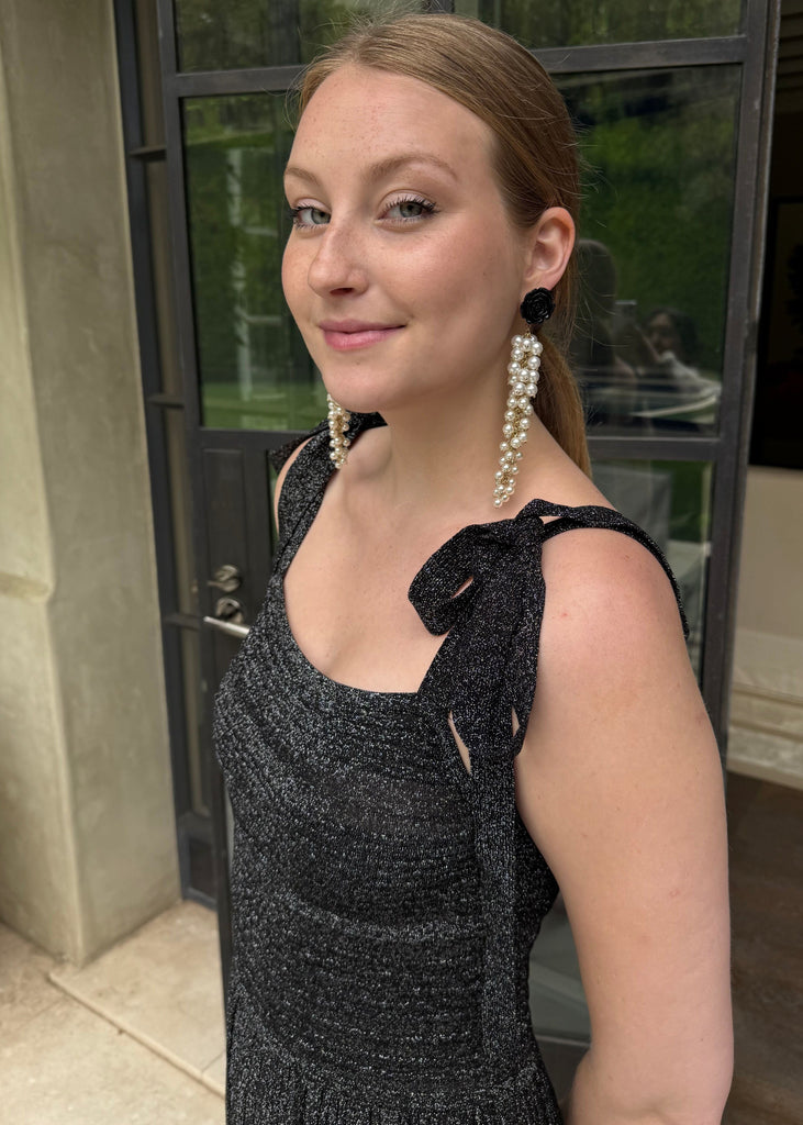 Woman wearing a black dress with a bow detail and pearl earrings, standing outdoors.