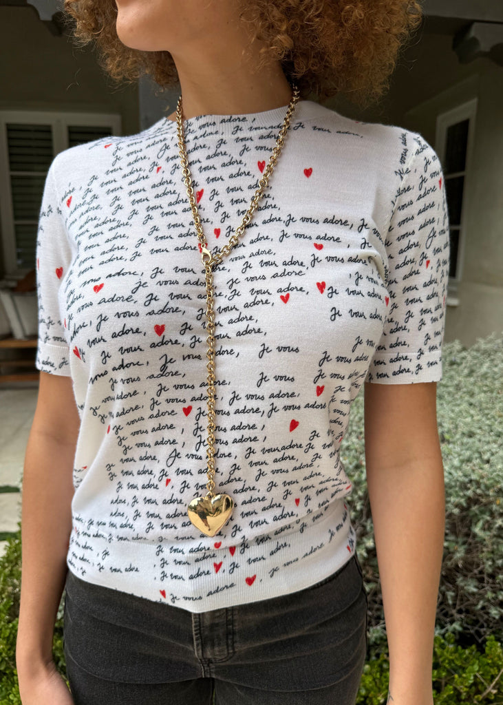 Person wearing a white t-shirt with text and red hearts, standing outdoors.