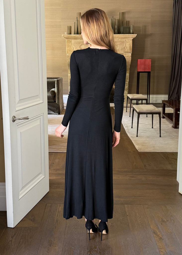 Woman in a black dress walking through a doorway into a room with a fireplace.
