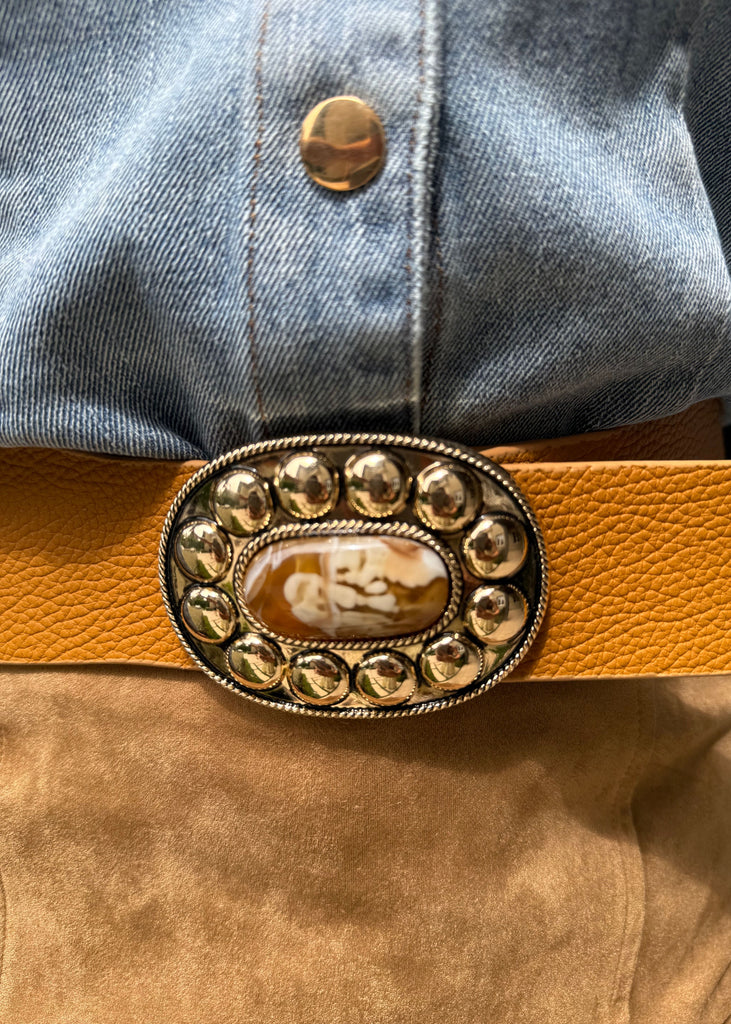 Yellow belt with decorative buckle worn by a person in a denim shirt.