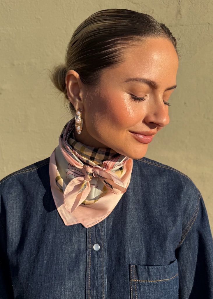 Woman wearing a patterned scarf around her neck against a beige wall.