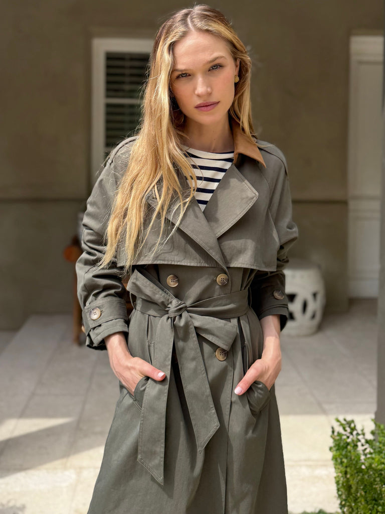 Woman wearing a gray trench coat standing outdoors with a neutral background