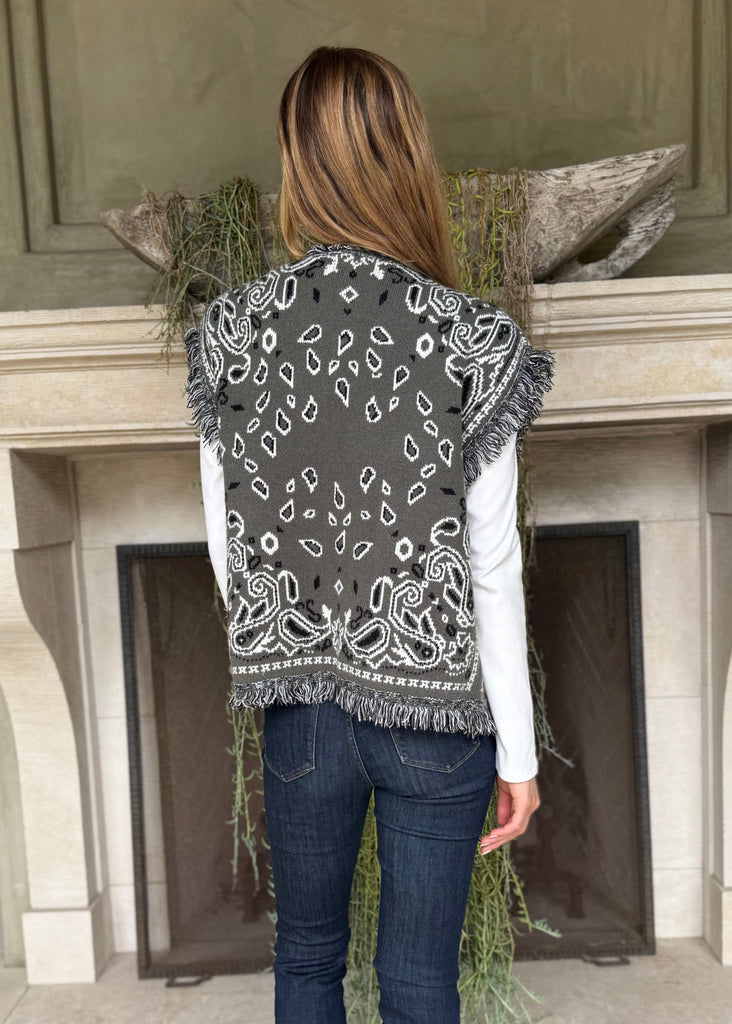 Person wearing a patterned vest standing in front of a fireplace.