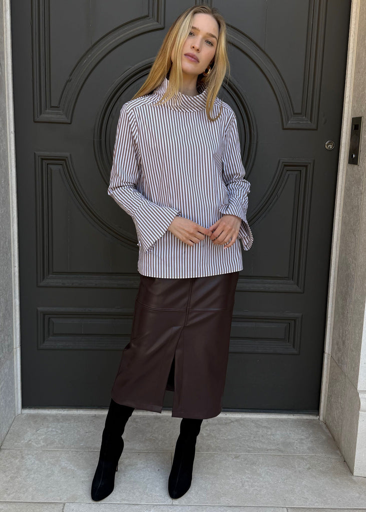 Woman standing in front of a large black door wearing a striped shirt and brown skirt.