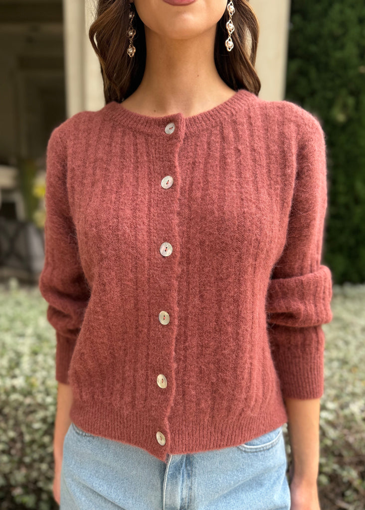 Person wearing a red knitted cardigan with a blurred outdoor background