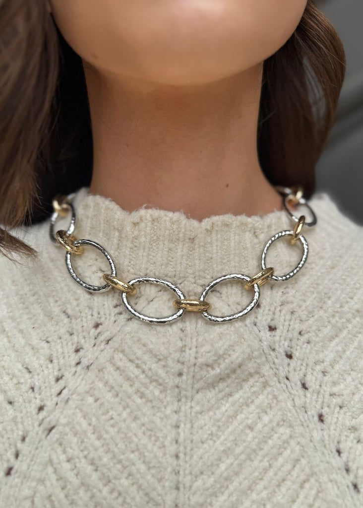 Necklace with gold and silver chain on a person wearing a light gray sweater.