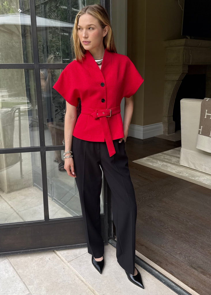 Woman in a red top and black pants standing in a doorway.