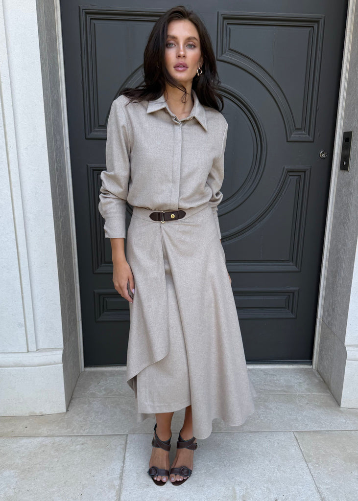 Woman in a beige outfit standing in front of a dark gray door.