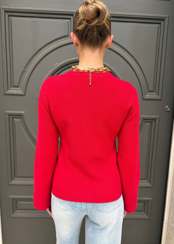 Person wearing a red sweater and light blue jeans standing in front of a gray door.