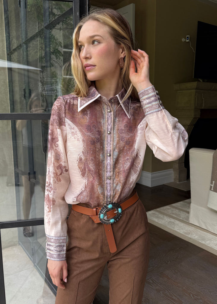 Woman wearing a patterned blouse and brown pants in an indoor setting