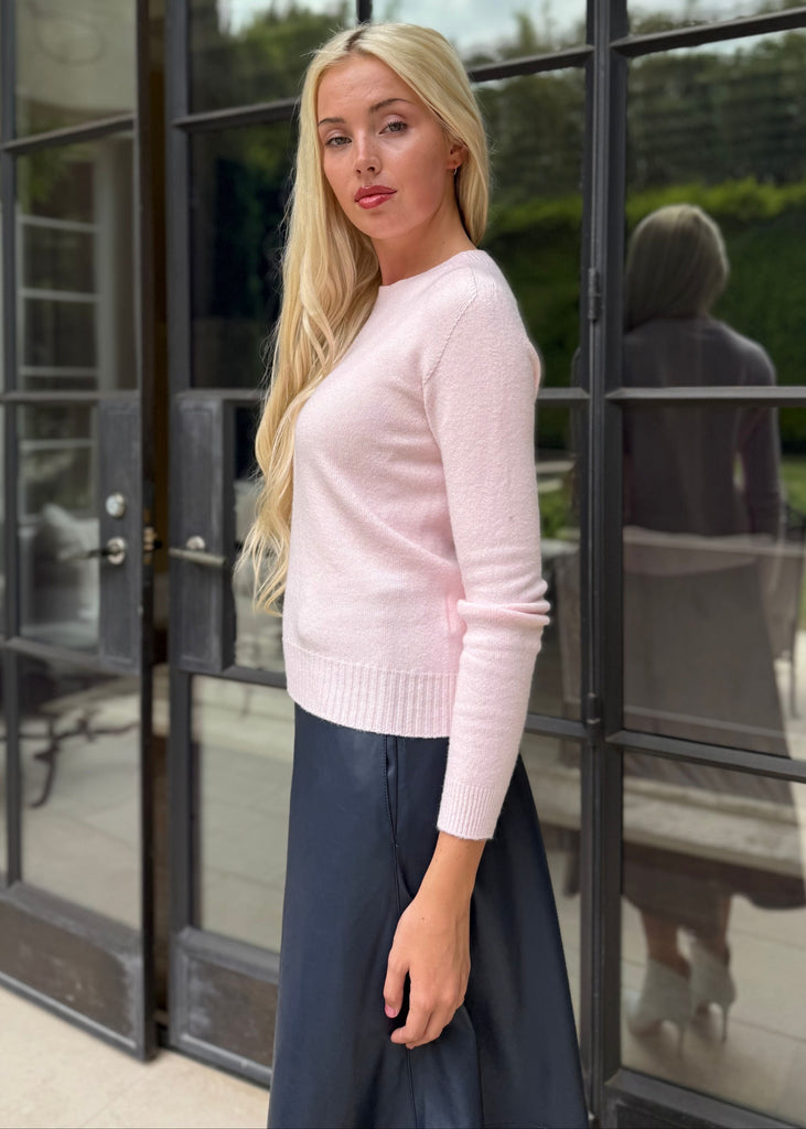 Woman in a pink sweater and dark skirt standing in front of a glass door.