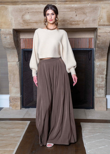 Woman wearing a beige sweater and brown pants standing in front of a fireplace.